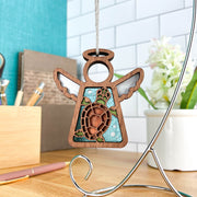 The Forged Flare® Sea Turtle Ornament, a 3.5" Mother's Angels® figurine with white wings and a sea turtle design, hangs on a metal stand—an ideal beach house accent for your desk near pens, books, a plant, and a white tiled wall.