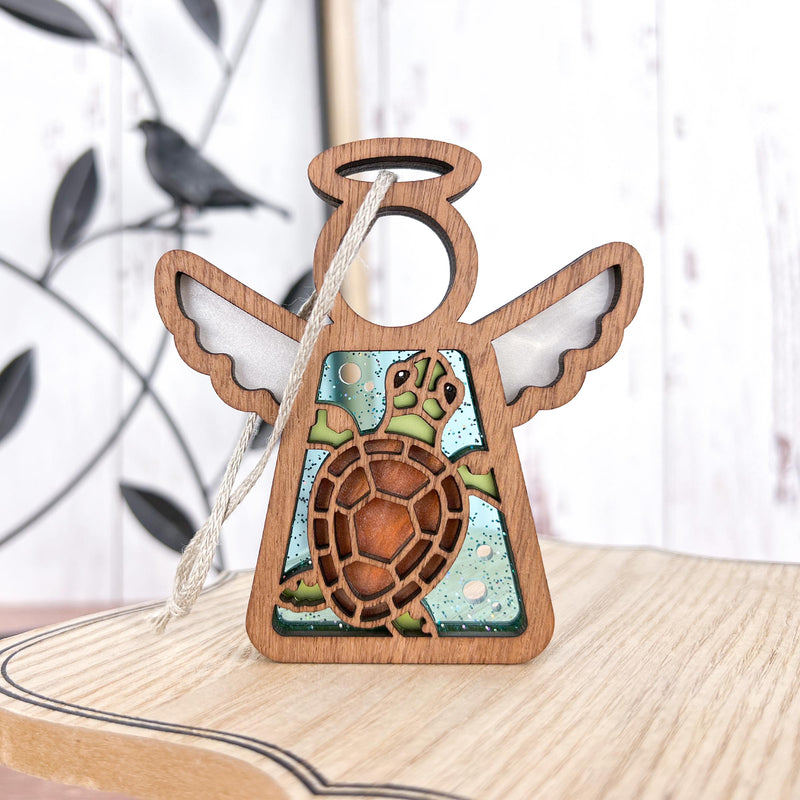 The Forged Flare® Sea Turtle with Imperfections Ornament is a 3.5" Mother's Angels® wooden angel figurine with white wings and a turtle cutout on a blue, speckled background—ideal as beach house decor or a Christmas tree ornament.