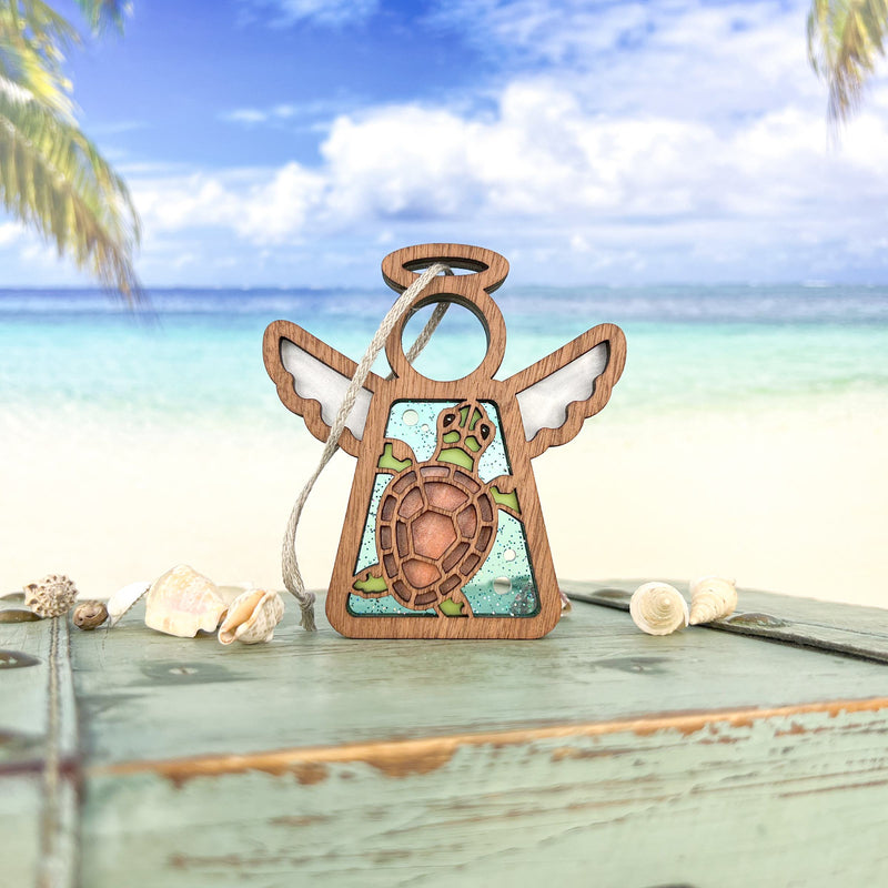 The Forged Flare® Sea Turtle Ornament (3.5" Mother's Angels® figurine) features teal accents and sits on a weathered green box with seashells, creating charming beach house decor with a tropical backdrop.