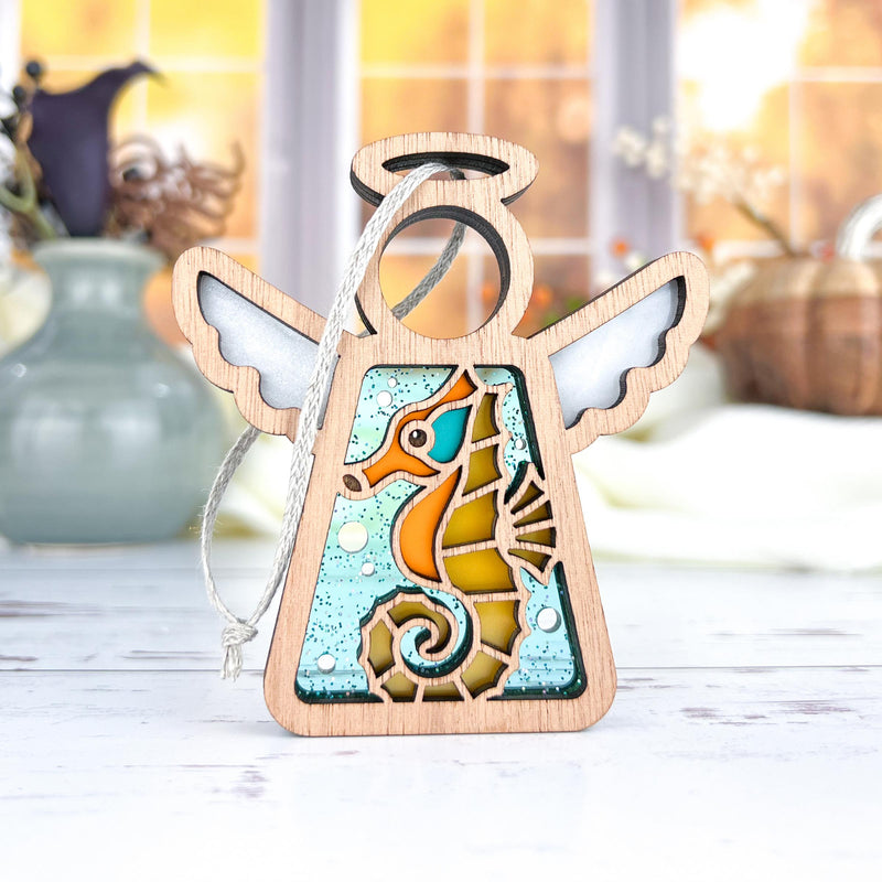 The Forged Flare® Seahorse Ornament is a 3.5" Mother's Angels® wooden angel figurine with outstretched wings and a stained-glass seahorse design—ideal as a Christmas tree ornament or beach house decor.