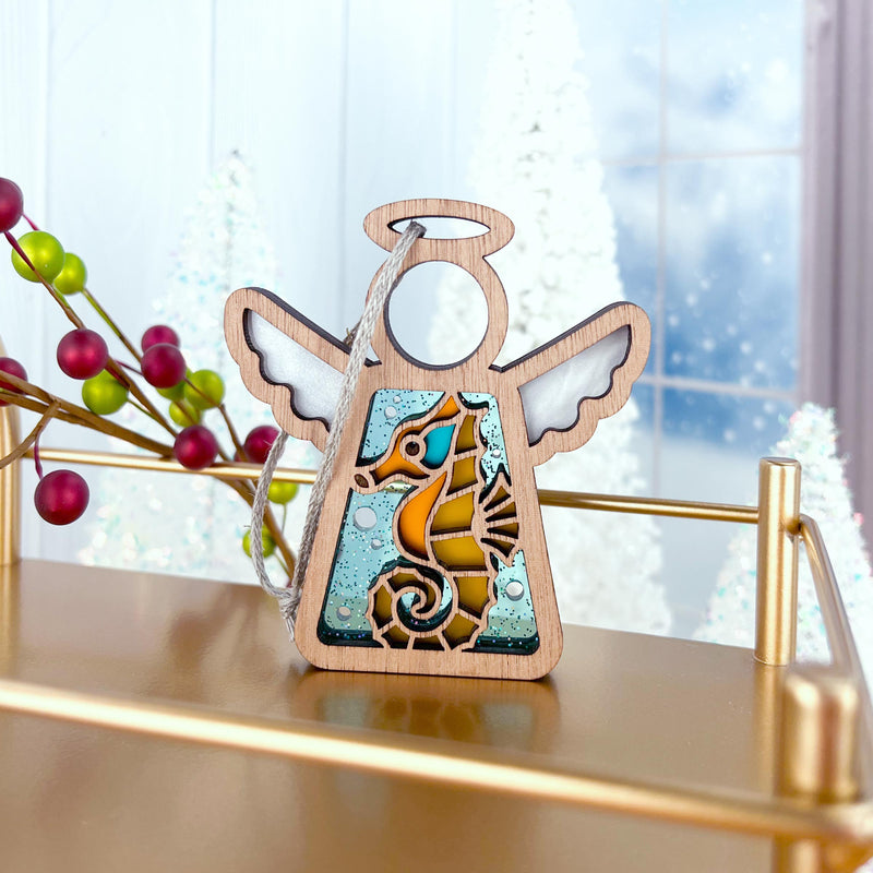 The Forged Flare® Seahorse Ornament is a 3.5" Mother's Angels® wooden angel figurine with translucent wings and a vibrant seahorse design, ideal as a unique Christmas tree ornament or beach house décor.