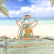 The Forged Flare® Mother's Angels® 3.5" Seahorse Ornament stands on a turquoise chest surrounded by seashells—a stunning beach house accent with a tropical ocean backdrop.