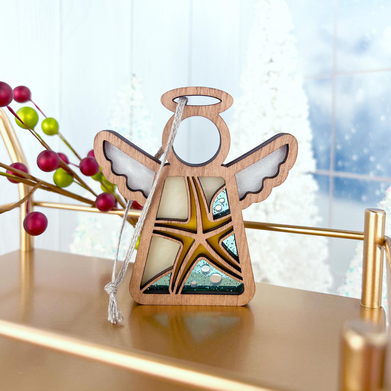 A Forged Flare® Starfish Ornament | 3.5" (H) Angel Figurine from the Mother's Angels® line adds coastal charm on a gold shelf, with festive red berries, frosted trees, and snowy window views enhancing the beach house holiday scene.