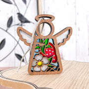 The Forged Flare® Mother's Angels® Strawberry Ornament is a 3.5" wooden angel figurine with white wings, a cutout strawberry and flower center, hanging on a string—perfect for your Christmas tree.