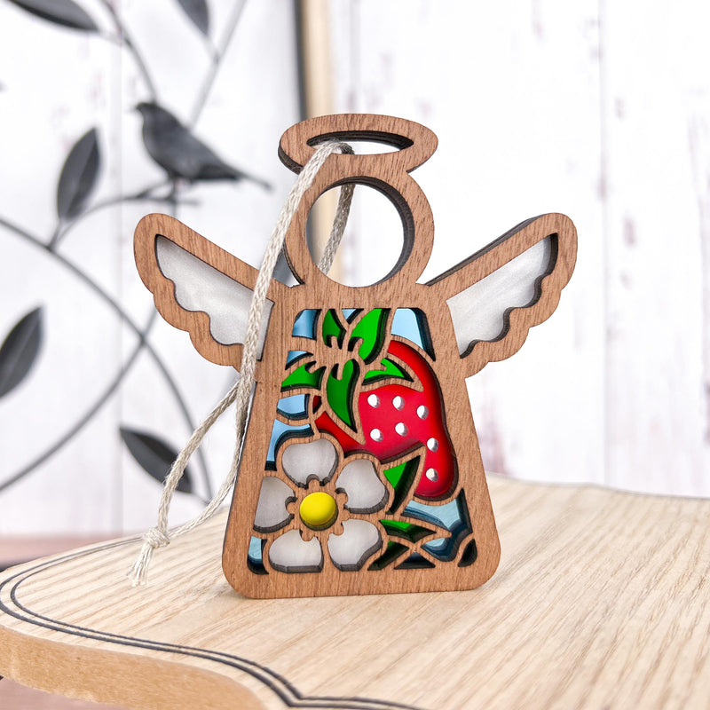 The Forged Flare® Mother's Angels® Strawberry Ornament is a 3.5" wooden angel figurine with white wings, a cutout strawberry and flower center, hanging on a string—perfect for your Christmas tree.