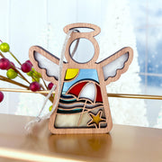 The Forged Flare® Mother's Angels® Summer Beach Ornament is a 3.5" wooden angel with stained glass-style insets featuring waves, a sunset, starfish, and sailboat. It hangs by a silver ribbon—an eye-catching Christmas tree decoration.