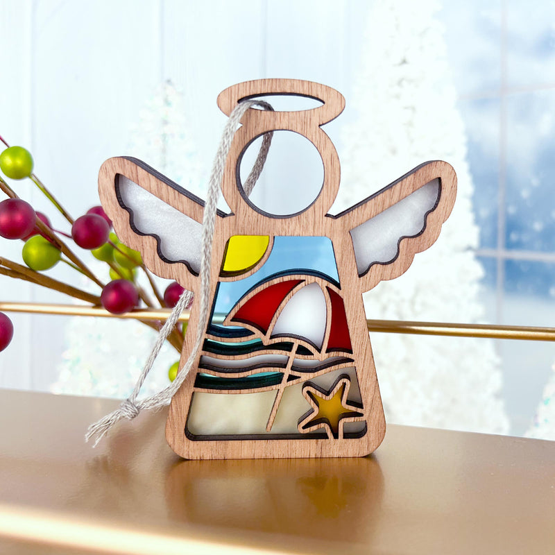 The Forged Flare® Mother's Angels® Summer Beach Ornament is a 3.5" wooden angel with stained glass-style insets featuring waves, a sunset, starfish, and sailboat. It hangs by a silver ribbon—an eye-catching Christmas tree decoration.