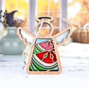 The Forged Flare® Summer Watermelon Ornament is a 3.5" Mother's Angels® figurine featuring stained glass-style red, green, and blue sections with white wings, displayed on a white surface with blurred vases and a window behind.