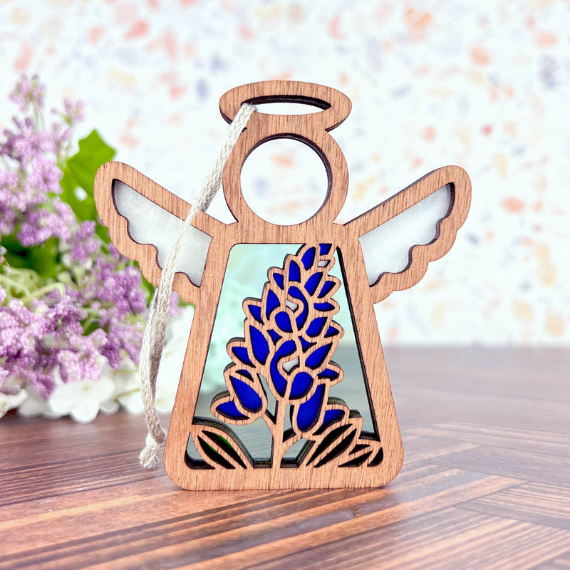 The Forged Flare® Texas Bluebonnet Ornament is a 3.5" wooden angel figurine from Mother's Angels®, featuring open wings, a central bluebonnet flower design, and a hanging string—perfect for flower décor enthusiasts.