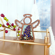 The Texas Bluebonnet Ornament by Forged Flare® is a 3.5" Mother's Angels® figurine, displayed on a gold tray amid festive berries and frosted trees—a lovely flower decor piece in a bright, wintry scene.