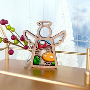 A Forged Flare® Mother's Angels® 3.5" angel figurine with stained glass wings and a colorful toadstool mushroom ornament stands on a gold shelf, framed by red berries, white Christmas trees, and a frosty window.