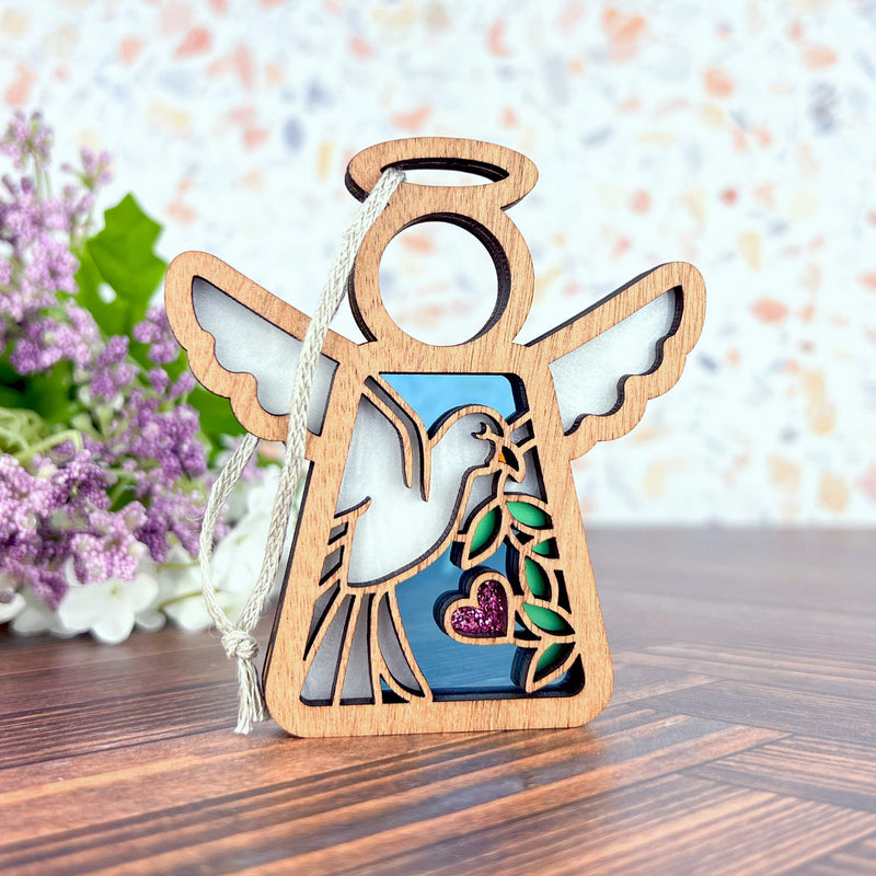 The Forged Flare® Mother's Angels® White Dove Ornament is a 3.5" wooden angel figurine with a dove and purple heart cutout—perfect as a memorial or bird lover gift. Shown on wood with lavender in the background.