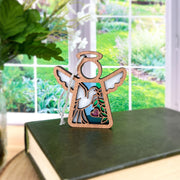 The Forged Flare® White Dove Ornament | 3.5" (H) Angel Figurine from the Mother's Angels® collection sits on a green book by a window, white flowers in the background—a thoughtful memorial gift for any bird lover.