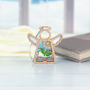 The Forged Flare® Mother's Angels® Book Lovers Ornament is a 3.5" wooden angel figurine with book, flower, and sun cut-outs—perfect as an author or book club gift—pictured on a light surface beside a closed book.