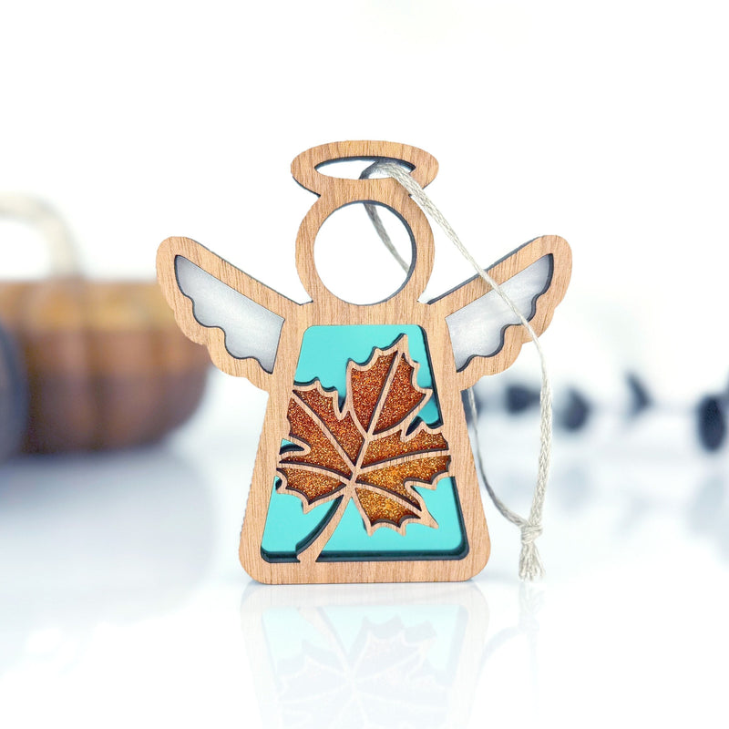 The Forged Flare® Mother's Angels® Sugar Maple Leaf for Charity Ornament is a 3.5" wooden angel with white wings, a turquoise body, and a glittery orange maple leaf center, inspired by the Appalachian Mountains and ready to hang.