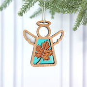 The Forged Flare® Sugar Maple Leaf for Charity Ornament | 3.5" (H) Angel Figurine by Mother's Angels® features a glittery orange maple leaf and turquoise center, hanging from a pine branch against a white background, inspired by the Appalachians.