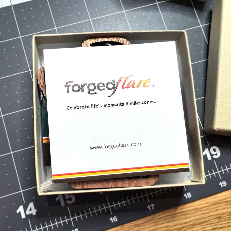 A square card displays the Forged Flare® logo, tagline "Celebrate life's moments & milestones," and website. The card is in a box, perfect for gifting the Warehouse Return - Swallowtail Butterfly Mother's Angels® Ornament.