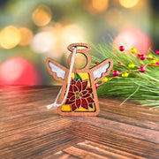 The PREORDERS CLOSED! Poinsettia Ornament is a 3.5" angel figurine from Mother's Angels® by Forged Flare®, featuring white wings and a red poinsettia design, displayed with festive pine branches and berries for a cozy holiday touch.
