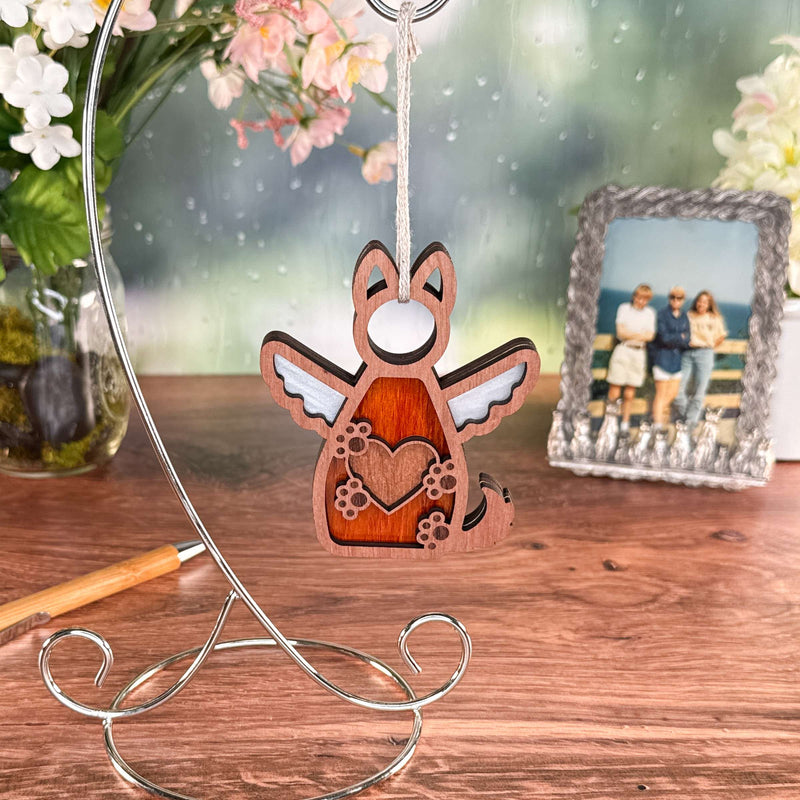 The Forged Flare® Forever By My Side Dog Angel Ornament features a wooden winged dog with a heart cutout on a stand, with flowers, pen, and framed photo in the background—an ideal dog lover gift or touching memorial.
