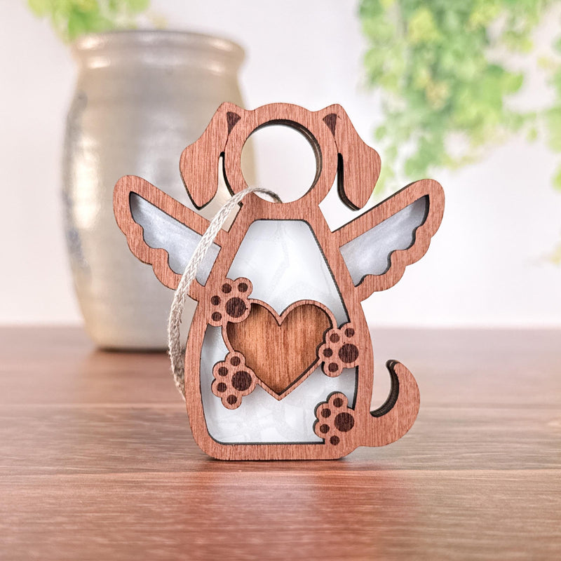 The Forged Flare® Forever In My Heart Dog Angel Ornament is a heartfelt wooden keepsake with wings and a heart, perfect as a dog lover gift or memorial. It includes a hanging loop, shown resting on wood with soft greenery in the background.