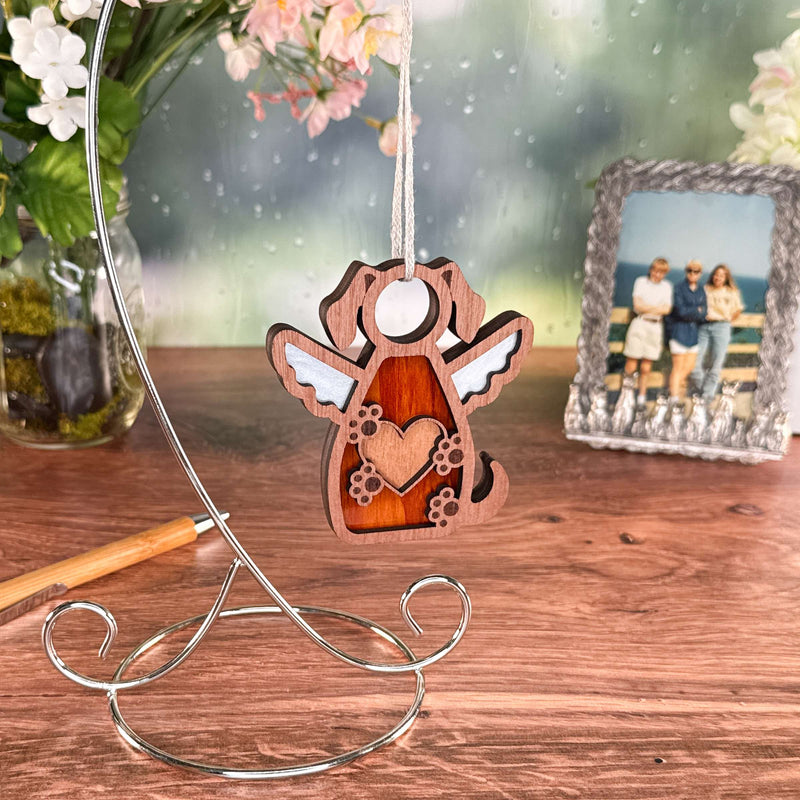 The Forged Flare® Forever In My Heart Dog Angel Ornament, featuring wings and a heart cutout, hangs from a metal stand—an ideal gift or heartfelt memorial for dog lovers.