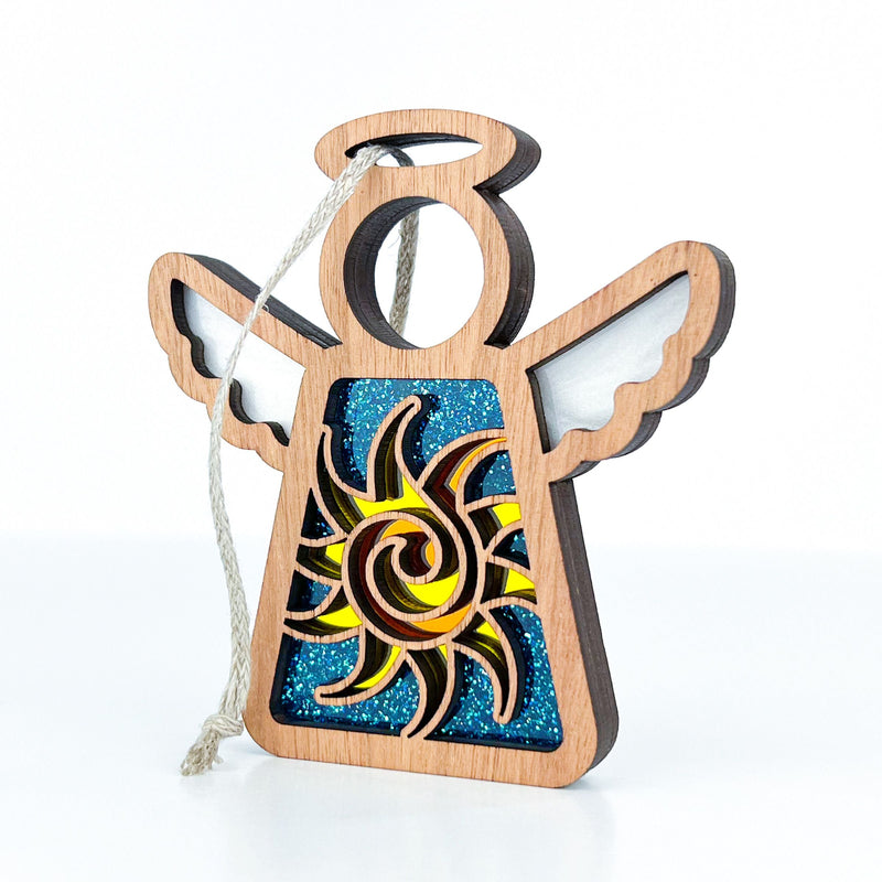 The Celestial Sun Ornament by Forged Flare® is a 3.5" Mother's Angels® figurine featuring cut-out wings and a sun design over a blue glittery background—perfect as a unique Christmas ornament or beach-themed gift.