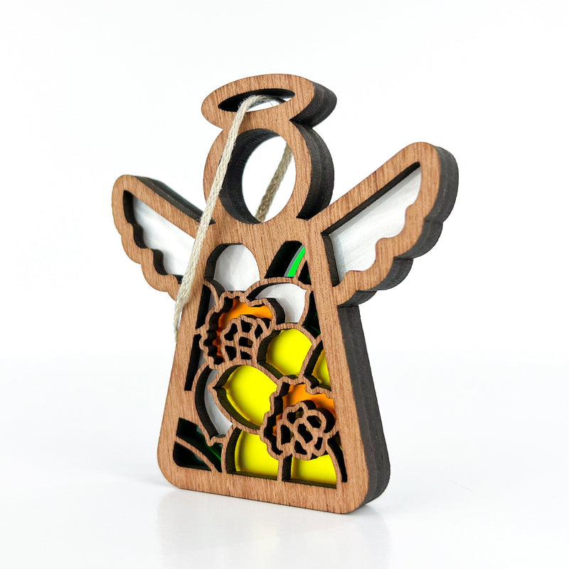 The Forged Flare® Mother's Angels® 3.5" Daffodil Ornament is a wooden angel figurine with white wings, a halo, yellow and orange daffodil details, and a string loop for hanging, shown on a white background.