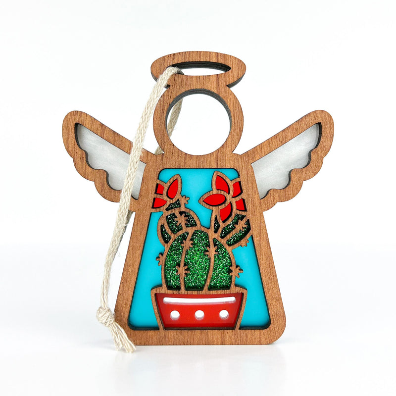 The Forged Flare® Desert Cactus Ornament is a 3.5" wooden angel figurine from Mother's Angels®, with a blue body, potted cactus, red flowers, and a white hanging cord—perfect for unique Southwest decor.