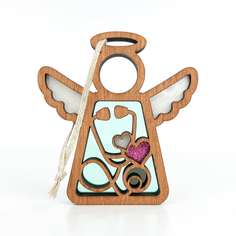 The Forged Flare® Mother's Angels® 3.5" Doctor/Nurse Ornament features cutout wings, a halo, and a white rope loop. Abstract shapes and a pink glittery heart accent the wooden angel despite minor imperfections.