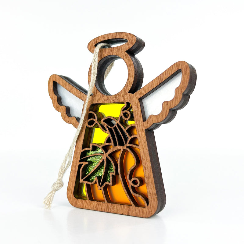 The Festive Pumpkin Ornament by Forged Flare® features a 3.5" angel figurine from the Mother's Angels® collection, with white wings and a yellow body adorned with intricate cut-out designs, including a palm tree. A string loop at the top makes it perfect for hanging as a Christmas tree ornament. Photographed in a plain white studio setting, it is an elegant addition to holiday décor.