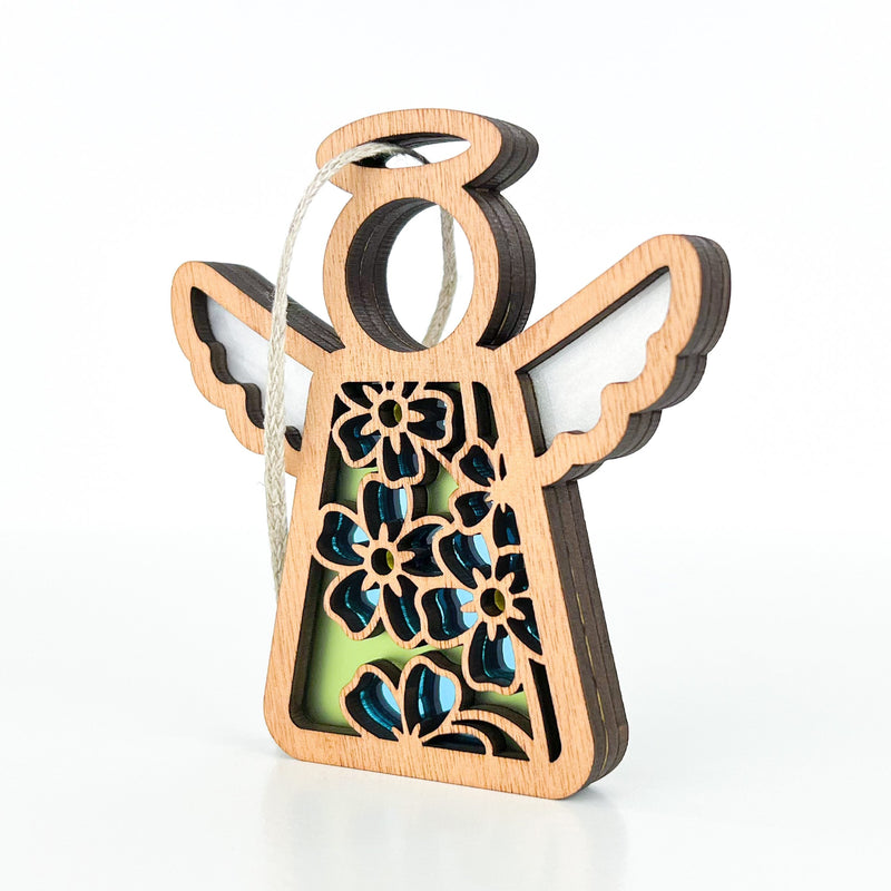 The Forget-Me-Not Ornament by Forged Flare® is a 3.5" wooden angel figurine with floral cutouts, blue and green accents, white wings, and a hanging loop—ideal for gifting or as décor. Features the Mother's Angels® design on a white background.