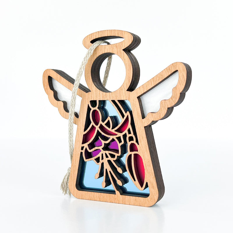The Fuchsia Ornament, a 3.5" (H) wooden angel figurine by Forged Flare® Mother's Angels®, features pink and blue cutout floral and abstract designs with a string loop—perfect as a charming Christmas tree ornament or thoughtful flower gift.