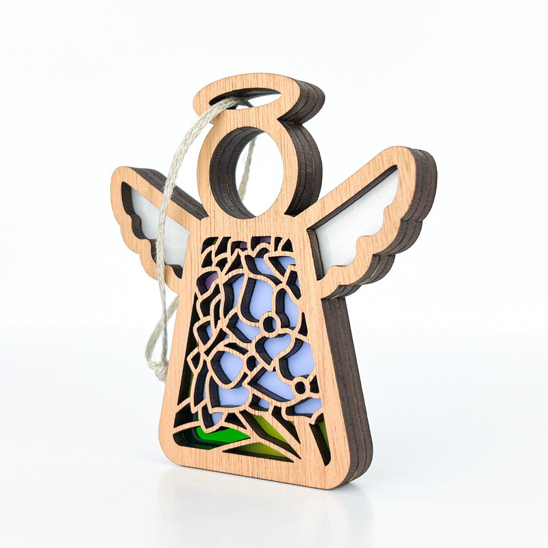 The Hydrangea Ornament by Forged Flare® is a 3.5" wooden Mother's Angels® angel figurine with a cutout floral pattern, colored acrylic accents, and hanging string, featuring detailed wings and dress against a white background.
