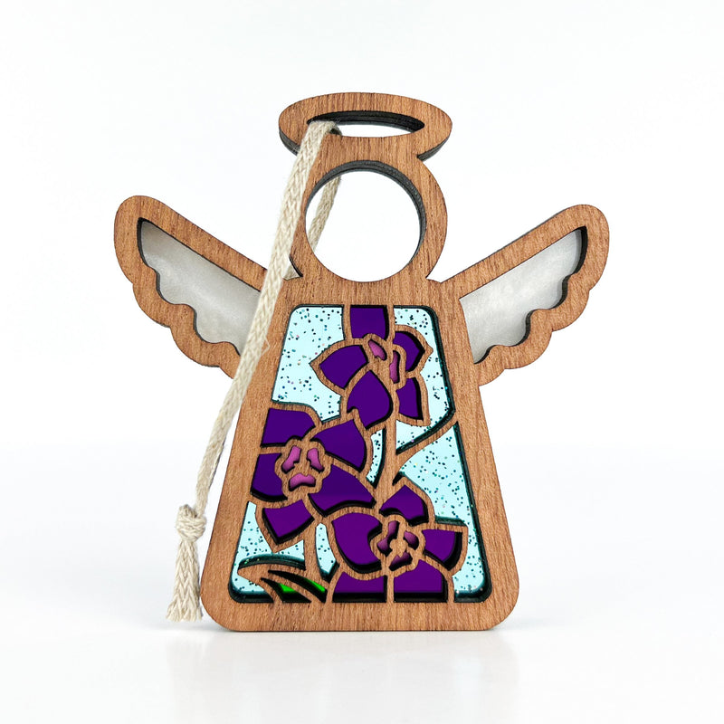 The Forged Flare® Larkspur Ornament is a 3.5" wooden angel figurine from Mother's Angels®, featuring stained glass-style wings, a purple larkspur (July birth flower) with green stems on blue, and a white hanging string.