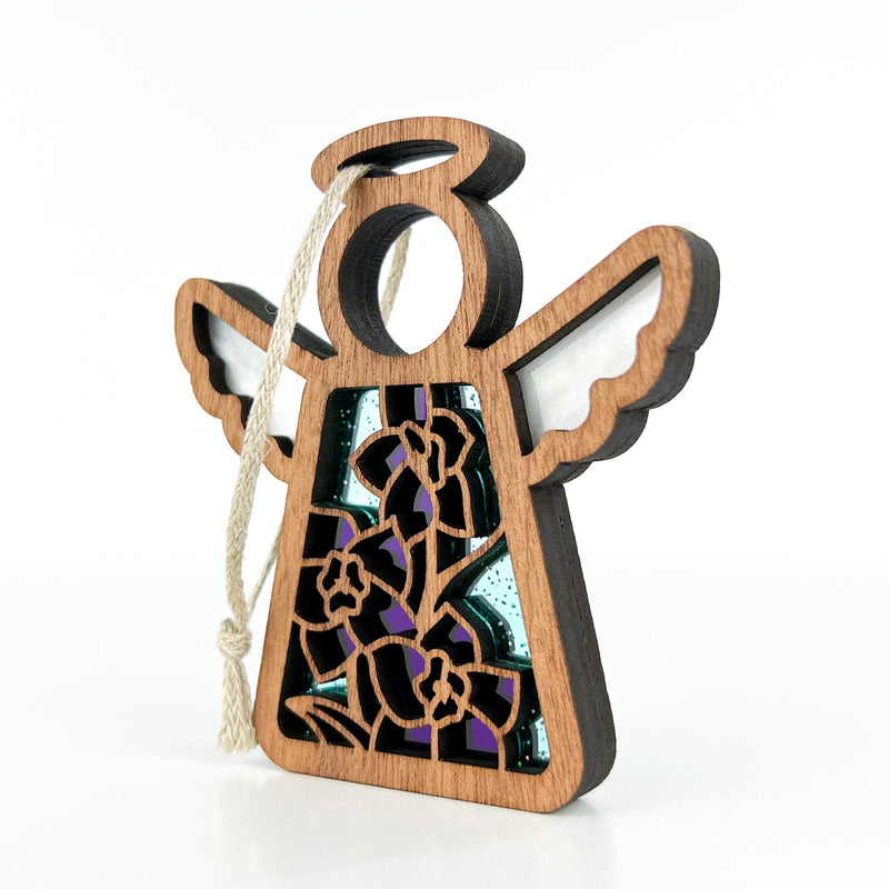 The Forged Flare® Larkspur Ornament is a 3.5" wooden angel with white wings, halo, and hanging string. Its stained glass body features purple larkspur—July’s birth flower—and yellow blooms on a vivid blue background.