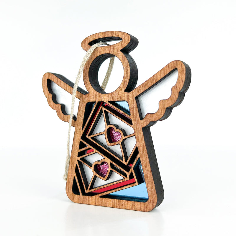 The Forged Flare® Letters of Love Ornament is a 3.5" wooden Mother's Angels® figurine with cut-out wings, glittery pink hearts, and a halo—ideal as a Christmas tree ornament or special mail carrier gift.