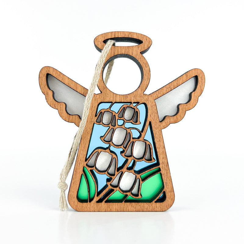 The Forged Flare® Lily of the Valley Ornament is a 3.5" Mother's Angels® wooden angel with a halo, blue and green stained-glass effect, white lily of the valley etching, and a cream string for hanging.