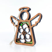 The Magnolia Ornament by Forged Flare® is a 3.5" angel figurine from the Mother's Angels® collection. This wooden angel features open wings, a halo, and a cutout flower design that reveals green glitter behind it. Ideal for Christmas tree decoration, it comes with a loop of white string for easy hanging.