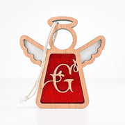 The Forged Flare® Personalized G Monogram Ornament is a 3.5" wooden angel figurine by Mother's Angels®, featuring cut-out wings, a red glittery center, gold script "G," and a white string for hanging—ideal for Christmas décor.
