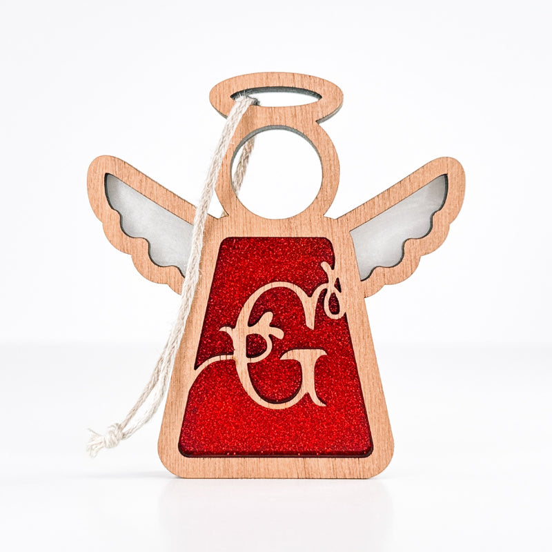 The Forged Flare® Personalized G Monogram Ornament is a 3.5" wooden angel figurine by Mother's Angels®, featuring cut-out wings, a red glittery center, gold script "G," and a white string for hanging—ideal for Christmas décor.