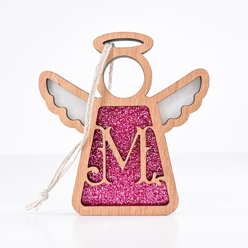 The Forged Flare® Mother's Angels® 3.5" Personalized M Monogram Ornament features a wooden angel with pink glitter, a monogram M, white wings, and a hanging loop, shown against a plain white background.
