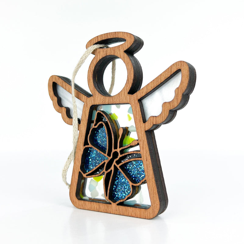 The Forged Flare® Mother's Angels® Morpho Blue Butterfly Ornament is a 3.5" wooden angel with white wings, a blue glitter butterfly at its center, and a hanging loop—shown on a plain white background.
