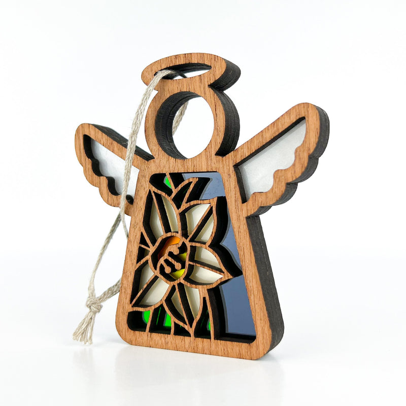 The Forged Flare® Narcissus Ornament is a 3.5" wooden Mother's Angels® figurine with white wings, halo, and a cut-out narcissus design—December’s birth flower—colored inlays, and a hanging loop. For plain white backgrounds.