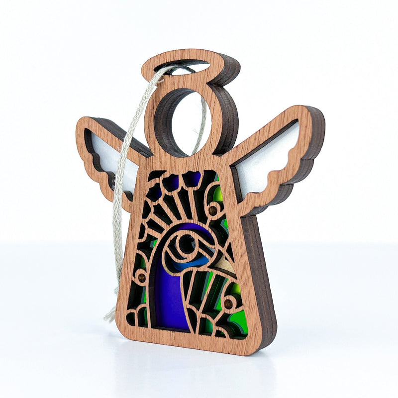 The Forged Flare® Peacock Ornament is a 3.5" Mother's Angels® figurine with white wings and stained glass-style blue-green accents, perfect as a bird lover gift or unique ornament, complete with a hanging string.