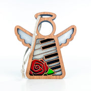 The Piano & Rose Ornament with Imperfections by Forged Flare® is a 3.5" handcrafted wooden Mother's Angels® figurine, featuring stained glass-inspired wings, piano keys, a red rose at the base, and a hanging string—perfect for collectors.