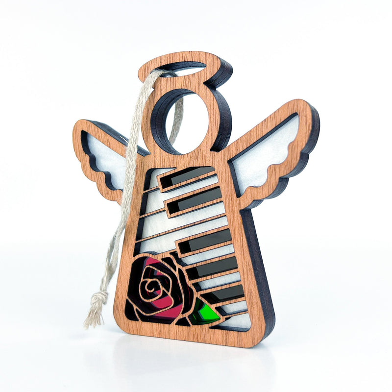 The Forged Flare® Piano & Rose Ornament with Imperfections is a 3.5" handcrafted Mother's Angels® figurine, featuring an angel with white wings, piano key details, a red and green rose, and a hanging loop—perfect for collectors.