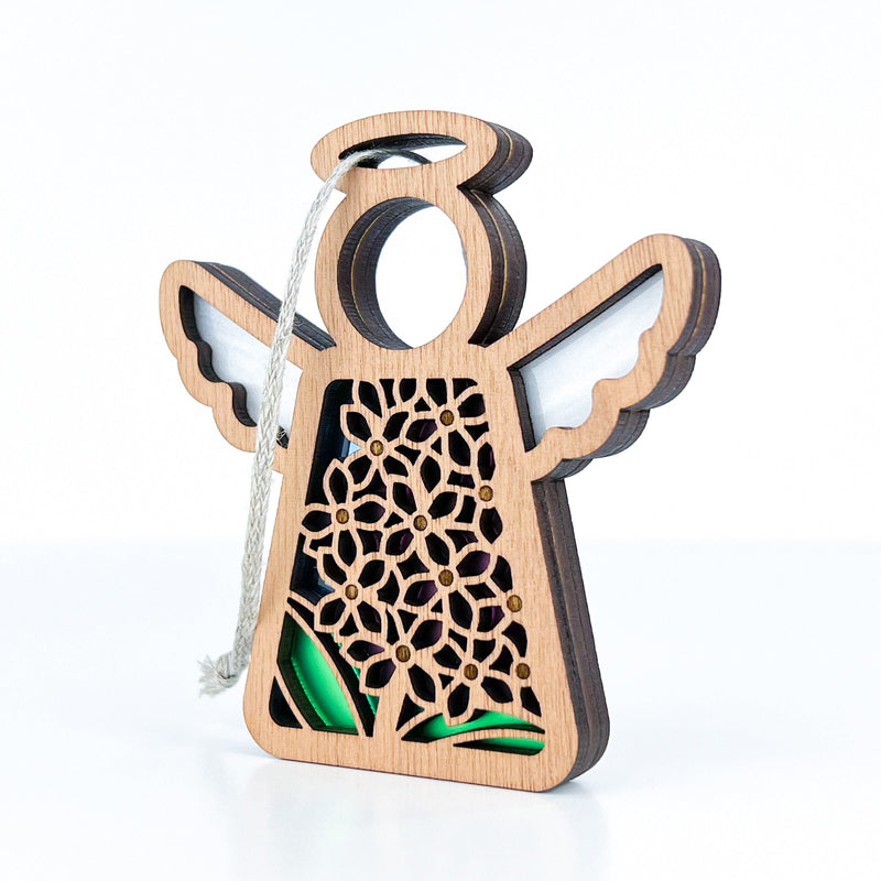 The Forged Flare® Mother's Angels® Purple Lilac Ornament is a 3.5" angel figurine featuring floral cutouts, white wings, a halo, and hanging string—an elegant Christmas tree decoration shown against a white background.