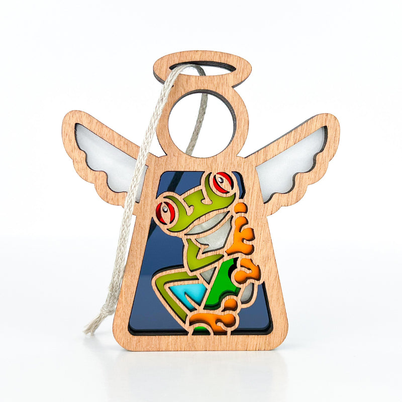 The Forged Flare® Red-Eyed Tree Frog Ornament is a 3.5" Mother's Angels® angel figurine with white wings, a cartoon-style frog, and a halo. Great as a frog gift or Christmas ornament, it includes a string loop for hanging. Plain white background.