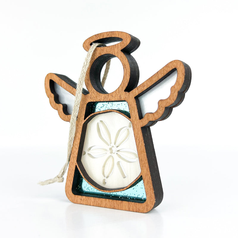 The Forged Flare® Mother's Angels® Sand Dollar Ornament with Imperfections is a 3.5" handcrafted angel figurine featuring open wings, a halo, rope hanging loop, and a sand dollar centerpiece set against a teal background.