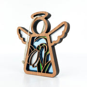 The Snowdrop Ornament, a 3.5-inch angel figurine from the Mother's Angels® collection by Forged Flare®, features a wooden design with outstretched wings and a delicate cutout of January's birth flower, the snowdrop, set against green leaves on a blue background. The ornament is gracefully suspended by a twine loop attached to the angel's head.